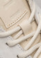 Close-up of V10 Leather Color Mix Beige low top sneakers with thick white laces and a textured label.