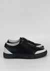 A pair of SO0010 Black & White low-top slip-on sneakers with white soles, displayed against a neutral gray background.