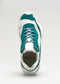 A front view of a white and teal low top sneaker with laces tied, featuring a prominent "V3 Leather Color Mix Emerald" brand label on the tongue.