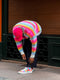 Person in a rainbow-striped sweater and red cap bending down to tie their colorful canvas shoes on a city street.