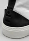 Close-up of the back heel of a TH0010 by Letícia shoe with a black suede accent and logo, set against a grey background.