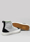 A pair of TH0018 by Joice high-top sneakers for women with white, black, and grey coloring, displayed against a plain grey background. Expertly handcrafted in Portugal from premium canvas, one shoe stands upright while the other lies on its side showing the sole.