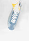A person wearing the V1 Antique White sneaker, crafted from premium canvas, along with a white sock featuring a yellow tie-dye pattern, stands against a light background.