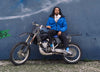  Ein Mann auf einem Motorrad vor einer blauen Wand, der Diverge sneakers, Förderung sozialer Auswirkungen und maßgefertigter Schuhe im Rahmen des IMAGINE-Projekts.