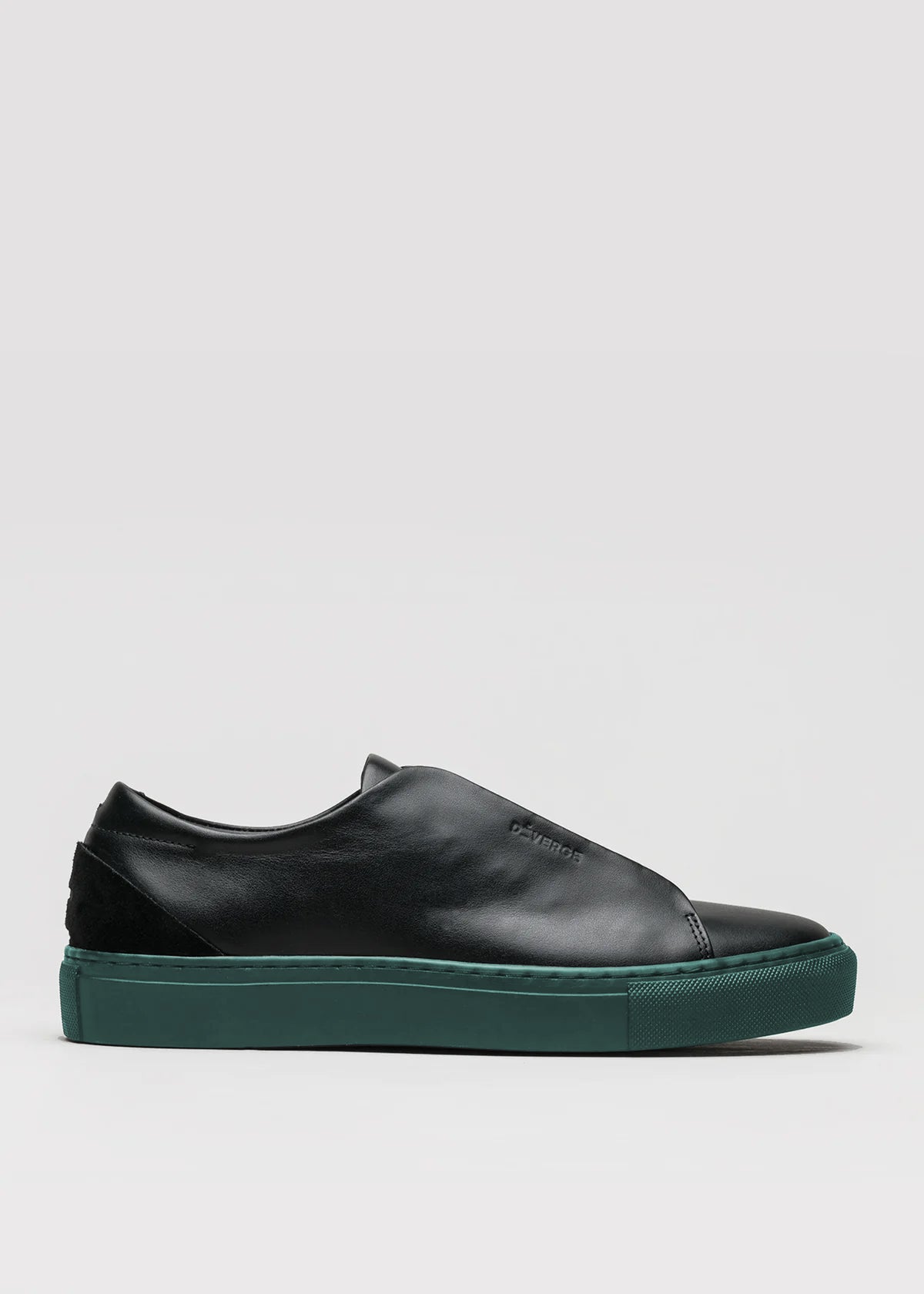 The V49 Black w/ Forest Green is a Minimal Low slip-on sneaker featuring premium Italian leather, a dark green sole, and a subtle embossed logo on the side, handcrafted in Portugal against a plain light gray background.