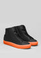The V48 Black W/ Orange sneakers, handcrafted in Portugal, feature premium Italian leathers and bright orange soles against a gray backdrop.