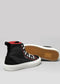 The TH0022 by João is a pair of handcrafted high-top sneakers from Portugal, featuring a gray background with black design elements, white laces and soles, and red accents. One sneaker stands upright while the other rests on its side, showcasing the intricate tread pattern.