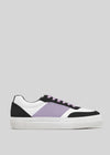 The N0019 by Ana Júlia is a handcrafted low-top sneaker from Portugal, featuring a white sole, black and white panels, and a purple stripe. Made from premium Italian leathers, it includes purple laces and showcases a minimalist design on a gray background.