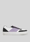 The N0019 by Ana Júlia is a handcrafted low-top sneaker from Portugal, featuring a white sole, black and white panels, and a purple stripe. Made from premium Italian leathers, it includes purple laces and showcases a minimalist design on a gray background.