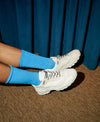 A person wearing blue socks with white low top custom sneakers by Diverge.