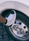 A person wearing TH0018 by Joice, handcrafted in Portugal using high-quality materials, rests their foot on the tire of a white vehicle.