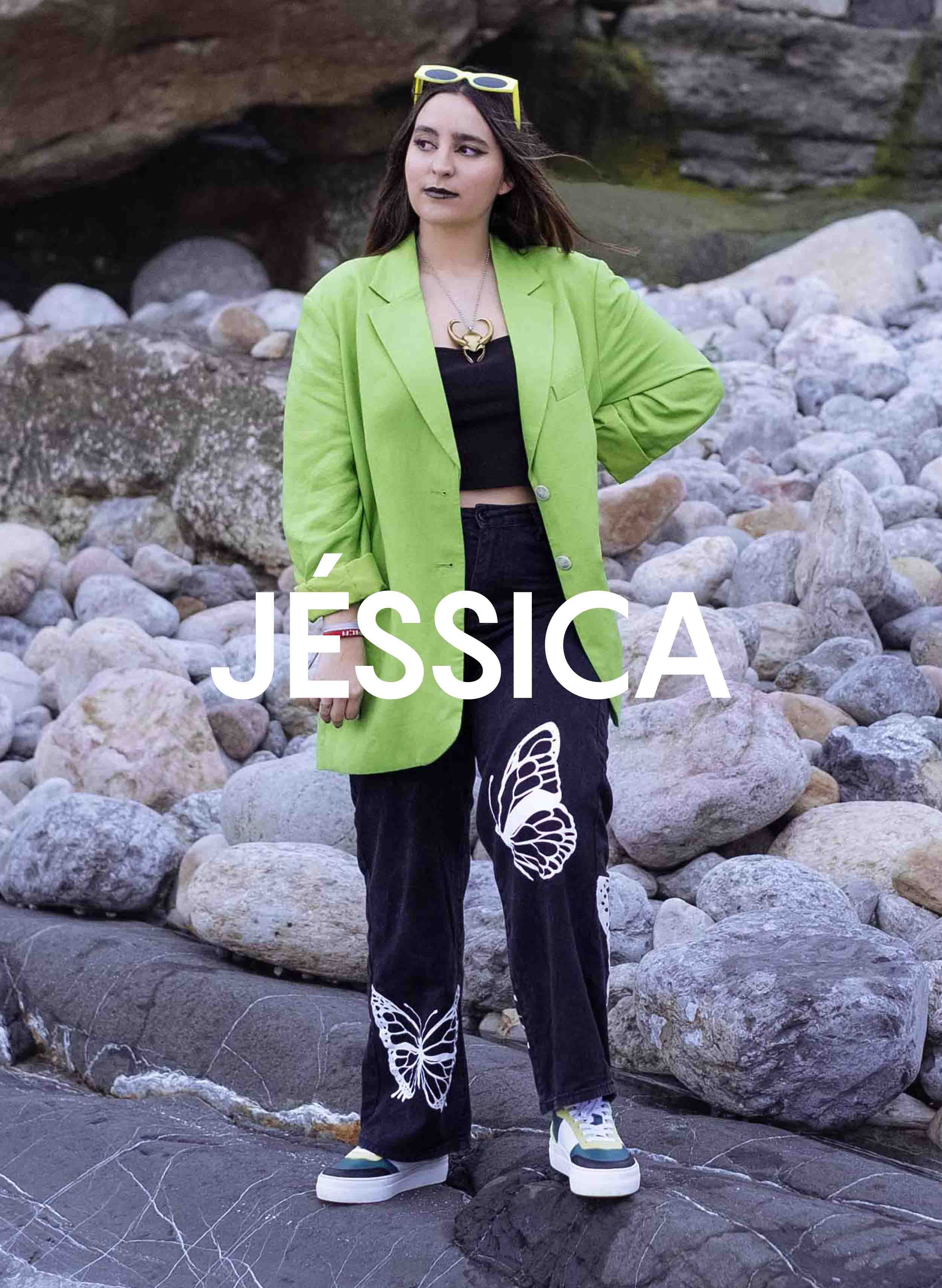 Jessica, con una chaqueta verde y pantalones negros, de pie sobre las rocas, Diverge sneakers, promoviendo el impacto social y el calzado personalizado a través del proyecto Imagine.