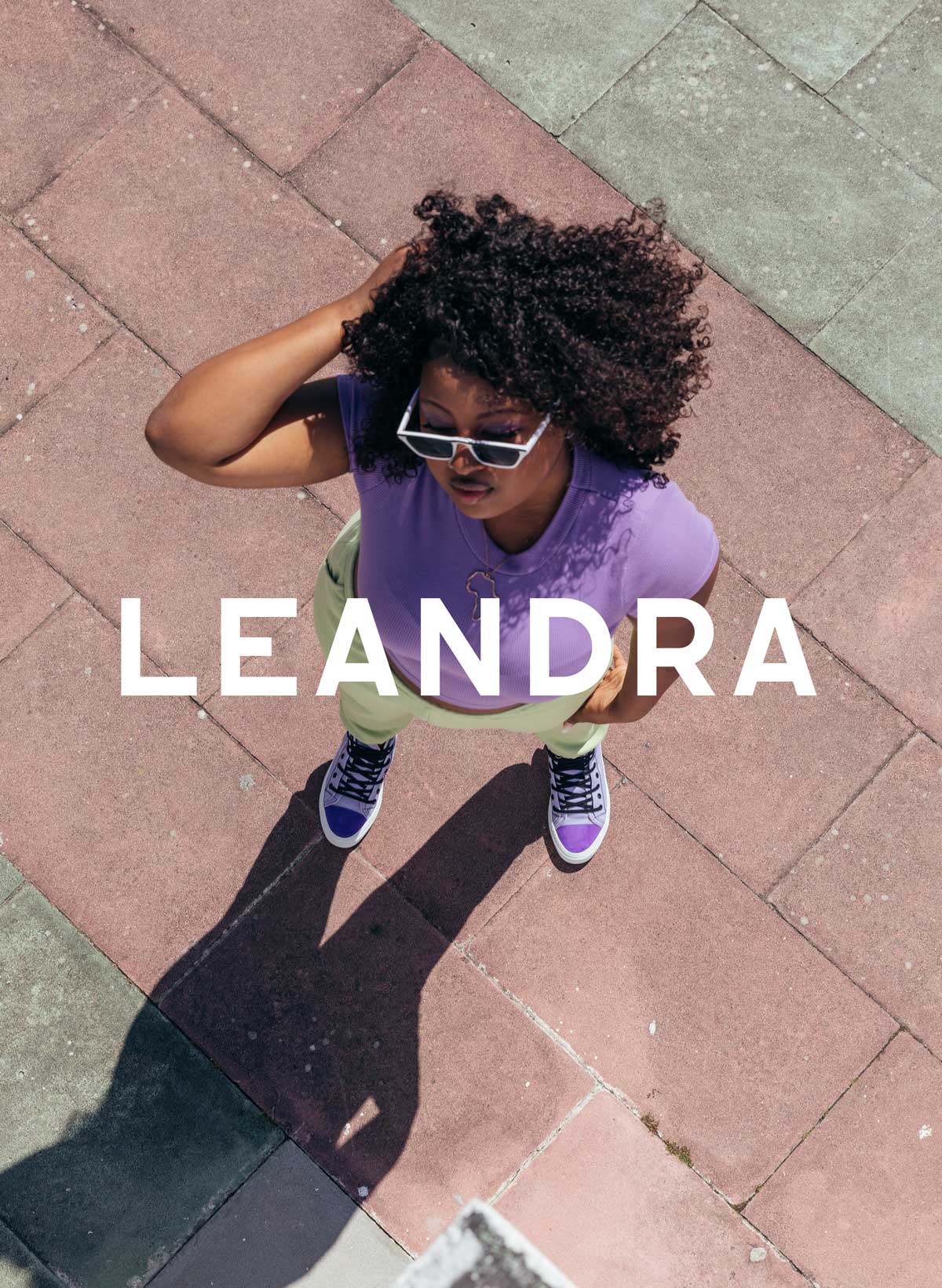 Leandra en chemise violette et lunettes de soleil debout sur un trottoir, portant Diverge sneakers, promouvant l’impact social et les chaussures personnalisées à travers le projet Imagine.