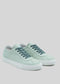 The V6 Sage Green sneakers, meticulously handcrafted in Portugal with dark green laces and durable white rubber soles, are artfully displayed against a minimalist gray backdrop.