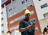 Un hombre con sombrero amarillo y camisa negra, concentrado en su teléfono , vistiendo Diverge sneakers , destacando el impacto social y el calzado personalizado a través del proyecto imagine.