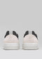 The V29 Bone & Black sneakers, handcrafted in Portugal, feature Italian leather uppers in black and beige with white soles, seen from the back against a plain gray background.
