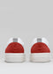 Due N0001 by Chrys low top sneakers con talloniere rosse e linguette grigie, su sfondo grigio.