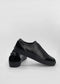Une paire de chaussures à enfiler SO0014 Black Floater à dessus texturé et semelles plates, présentées sur un fond blanc uni.