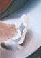 A person wearing N0017 by Raquel, showcasing beige pants and white sneakers with blue and white accents, crafted from premium Italian leathers, is standing on a shiny surface.