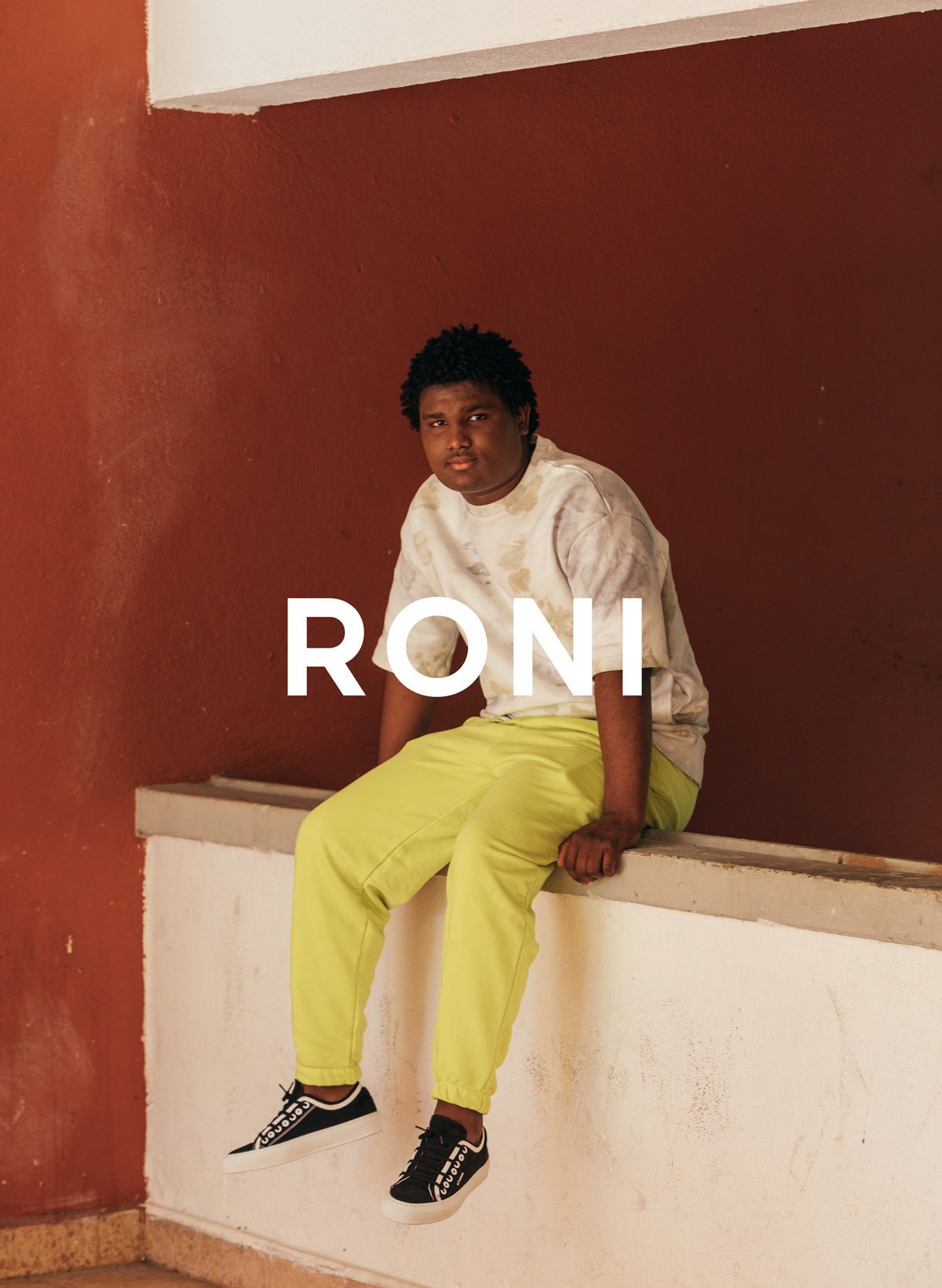 A man sitting on a ledge with custom shoes named Roni, showcasing Diverge sneakers and promote social impact throught the imagine project.
