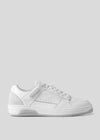 The V0 White sneaker, handcrafted in Portugal, showcases white premium Italian leather with a textured sole and side perforations. Finished with white laces, it exudes a retro-future vibe against a plain gray background.