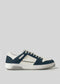 Crafted from premium Italian leathers, the V13 Deep Blue W/ Off White is a white and dark blue low-top sneaker featuring perforated side details, a textured rubber sole, and laces. Handcrafted in Portugal, it embodies timeless elegance and is set against a plain gray backdrop.