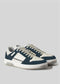 The V13 Deep Blue W/ Off White sneakers are retro-future low-tops crafted in Portugal with premium Italian leathers, featuring white soles, dark blue and white uppers, and white laces, set against a plain gray background.