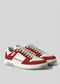 The V18 Off White W/ Scarlet sneakers, handcrafted with premium Italian leathers, feature white laces and rubber soles. Displayed against a plain gray backdrop, these shoes offer an elegant touch and contemporary flair.