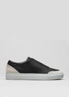 The V19 Black Leather W/ Bone sneaker is crafted in Portugal, featuring a slip-on design with a white sole and light gray suede detailing at the heel, set against a plain gray background.