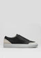 The V19 Black Leather W/ Bone sneaker is crafted in Portugal, featuring a slip-on design with a white sole and light gray suede detailing at the heel, set against a plain gray background.