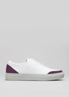 The V25 White W/ Plum is a handcrafted low-top sneaker made in Portugal from premium Italian leathers. It features a white design with plum accents on the toe and heel, a flat sole, and is set against a plain gray background.