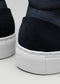 Close-up of two sneakers, V46 Blue Floater W/ White, with textured soles. Focus on the back heel section with a subtle embossed logo on black suede. Handcrafted in Portugal using premium Italian leathers, these shoes exemplify timeless style and quality craftsmanship.