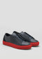 The V48 Deep Blue W/ Red sneakers are handcrafted in Portugal, featuring deep blue leather with distinctive red soles, showcased on a light gray background, facing forward and angled slightly to the right.