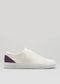 The V52 Off White W/ Plum, a white low-top sneaker with a plum heel accent handcrafted in Portugal from premium Italian leather, rests elegantly on a plain gray background.