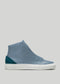 The V54 Lake W/ Petrol Blue is a handcrafted blue high-top sneaker made in Portugal, featuring a white sole and a teal suede heel accent, displayed against a light gray background.