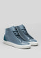 The V54 Lake W/ Petrol Blue are blue high-top sneakers featuring white soles and teal suede heel accents. Handcrafted in Portugal from premium leather, they are showcased against a plain gray background.