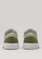 The V54 Sage Green W/ Olive sneakers are shown from the back, featuring a beige color with white soles. Crafted from premium Italian leathers, they have minimal circular and rectangular designs on the heel. Handcrafted in Portugal, they rest against a plain light gray background.