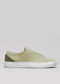 The V54 Sage Green W/ Olive sneaker, handcrafted in Portugal with premium Italian leathers, is showcased from the side. Its light green tones elegantly contrast with a white sole against a plain gray background.
