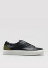 The V57 Black W/ Olive is a black leather slip-on low top sneaker featuring a white rubber sole and olive green heel detail. It's handcrafted in Portugal with premium Italian leathers and shown from the side against a plain background.