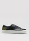 The V57 Black W/ Olive is a black leather slip-on low top sneaker featuring a white rubber sole and olive green heel detail. It's handcrafted in Portugal with premium Italian leathers and shown from the side against a plain background.