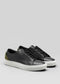 The V57 Black W/ Olive low-top sneakers feature a sleek black design with dark green heel accents and white rubber soles. Crafted from premium Italian leathers, one shoe has visible laces while the other conceals them, all expertly handcrafted in Portugal for unmatched style and quality.