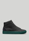 Der MH0011 YouNoMe II ist ein High-Top-Ledersneaker mit strukturiertem Absatz und auffälliger grüner Sohle auf einfarbig grauem Hintergrund.