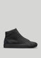 Una singola sneaker alta in tela nera MH0014 Pyck's Kicks con superficie in pelle liscia e dettagli in pelle scamosciata sul tallone, su uno sfondo grigio chiaro.
