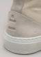 Primo piano di una sneaker V4 Antique White Canvas che mostra il tessuto testurizzato e il logo in rilievo sulla linguetta del tallone in pelle scamosciata sopra una suola in gomma bianca.