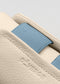 Primer plano de una cartera V16 de piel beige con lima, con interior de tela azul y la palabra "deverge" grabada en relieve, junto a un par de zapatos personalizados.