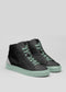 A pair of MH00019 Black Cat with a black upper and pastel green soles, featuring green laces against a plain gray background.