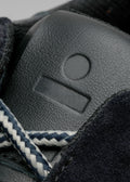 Primer plano de una zapatilla baja V7 Leather Color Mix Black con intrincados detalles, que incluyen un estampado texturizado, cordones cosidos en blanco en contraste y un indicador de talla visible.