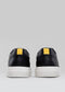 Une paire de V14 Vegan Black sneakers avec des semelles blanches et une boucle en tissu jaune sur le talon, présentée sur un fond gris.