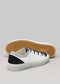 Une paire de TL0003 by Thierry low-top blanches sneakers avec des accents noirs et un motif nid d'abeille distinctif sur la semelle, présentée sur un fond gris.