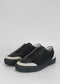 Une paire de SO0010 Black & White slip-on sneakers avec des semelles blanches sur un fond gris clair uni.